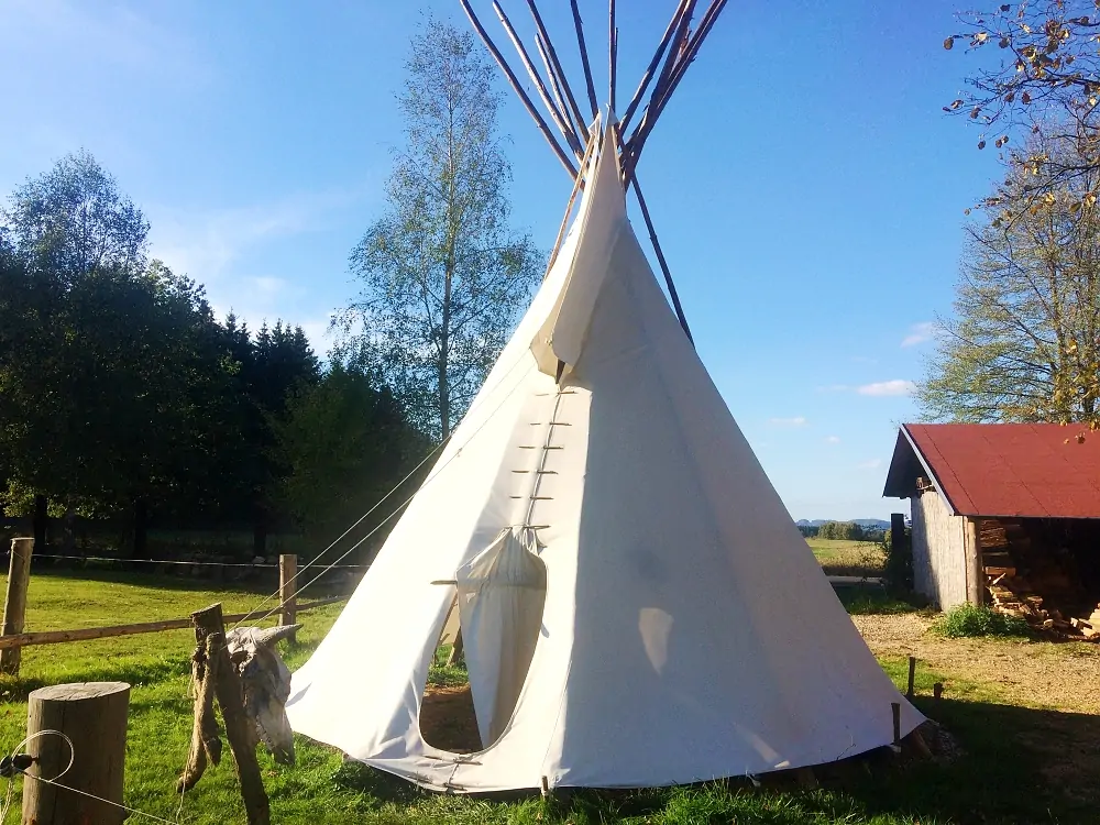 Bílé teepee na louce u usedlosti